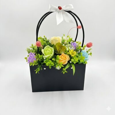 Un aranjament floral artificial multicolor într-o geantă neagră, decorat cu o panglică albă și o buburuză decorativă.