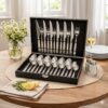 Set de tacâmuri din inox cu 24 de piese, așezate într-o cutie de prezentare neagră, design modern și elegant.