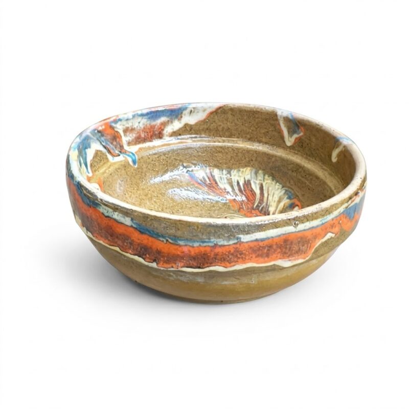 Bol din ceramică rustică lucrat manual cu glazură în nuanțe de portocaliu, albastru și maro, fundal alb.