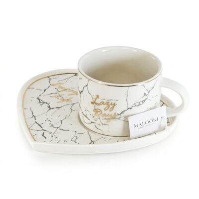 O cană de cafea din ceramică albă cu model de marmură și text auriu "Lazy Days", stând pe o farfurioară asortată.