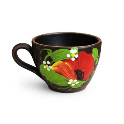 Cană din ceramică închisă la culoare, pictată manual cu motive florale, reprezentând o floare roșie și frunze verzi, pe fundal alb.