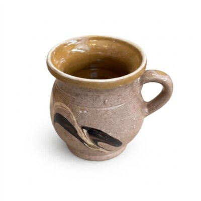 Cană tradițională din lut smălțuit, prevăzută cu toartă, decorată cu motive abstracte maro pe un fundal bej-nisipiu.