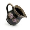 Carafă din ceramică neagră, cu o capacitate de aproximativ 750 ml, decorată cu un model elegant de trandafiri mov și frunze aurii, și o margine și un mâner cu glazură texturată granulată, izolată pe un fundal alb.