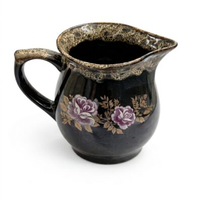 Carafă din ceramică neagră, cu o capacitate de aproximativ 750 ml, decorată cu un model elegant de trandafiri mov și frunze aurii, și o margine și un mâner cu glazură texturată granulată, izolată pe un fundal alb.
