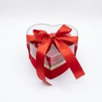 Aranjament floral în cutie în formă de inimă cu trandafiri roșii din material textil de mătase și fundă satinată, fundal alb pur.