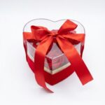 „Cutie transparentă în formă de inimă cu trandafiri roșii și fundă elegantă, ideală ca un cadou romantic.”