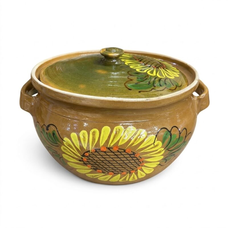 O oală tradițională, lucrată manual din ceramică de lut, cu un model vibrant pictat manual cu floarea-soarelui pe partea frontală. Oala are două toarte laterale mici și un capac verde-oliv asortat cu un motiv floral mai mic. Textura este a ceramicii artizanale, așezată pe un fundal alb curat.