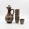 Set tradițional din ceramică maro cu modele în relief, format dintr-o carafă cu capac și șase cănițe, prezentat pe un fundal alb luminos pentru magazin online.