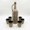 Set rustic din ceramică, format dintr-o sticlă cu dop de plută și 6 cănițe, cu design ce imită împletitura de nuiele, pe fundal alb.