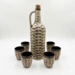 Set rustic din ceramică, format dintr-o sticlă cu dop de plută și 6 cănițe, cu design ce imită împletitura de nuiele, pe fundal alb.
