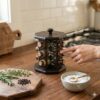 O persoană alegând un borcan din suportul rotativ pentru condimente din lemn, așezat pe un blat de bucătărie, alături de ierburi aromatice proaspete și un bol cu sare.